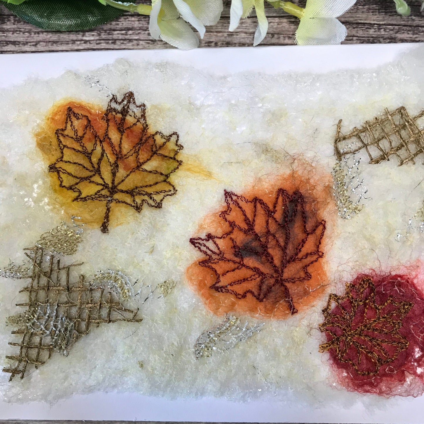 Carte de vœux avec trois feuilles d’érable jaune, orange et rouge brodée sur la laine