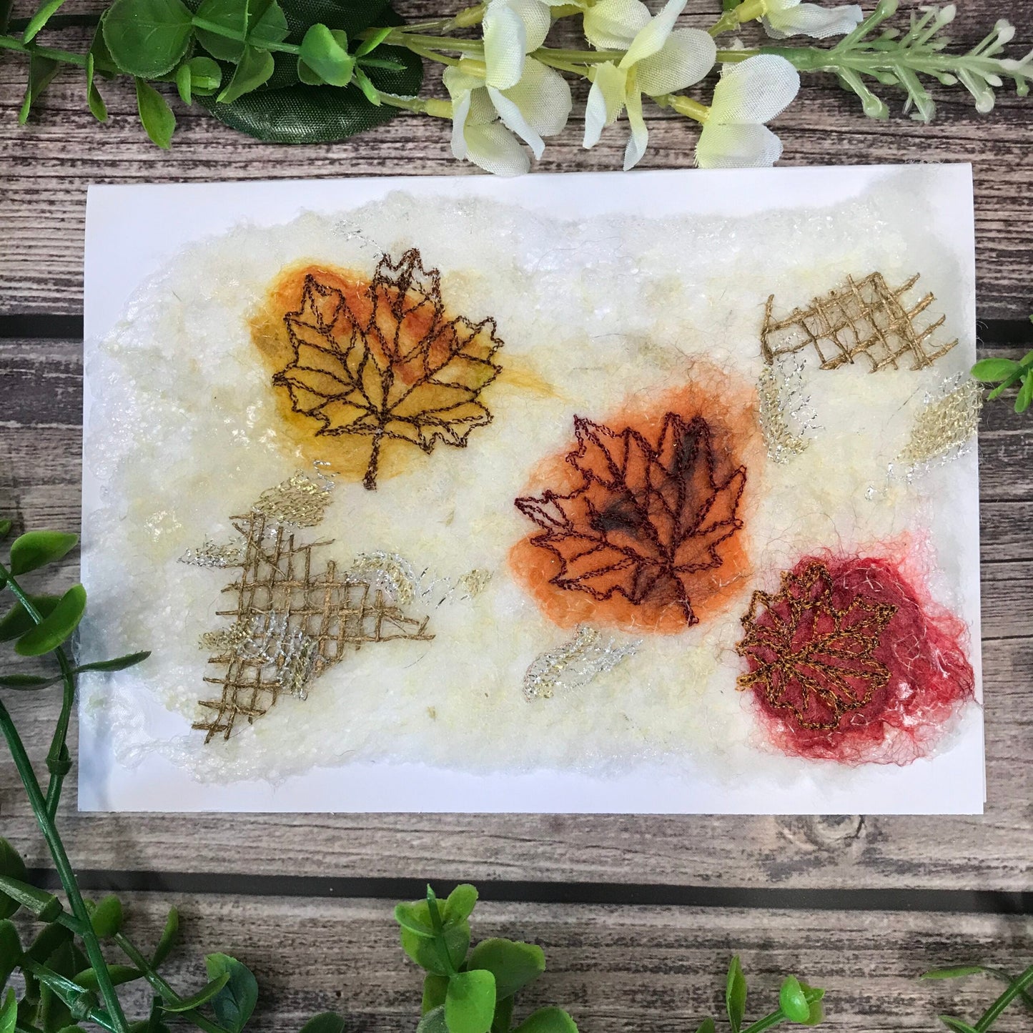 Carte de vœux avec trois feuilles d’érable jaune, orange et rouge brodée sur la laine